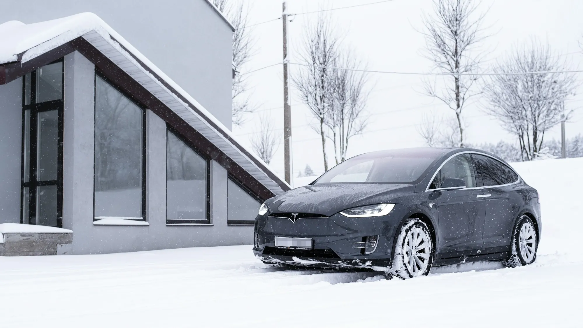 Tesla Model X parked in fresh snow outside a modern home